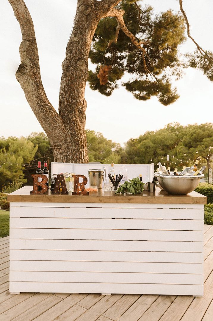 Destination wedding with whit wooden bar with rustic 'bar' sign 