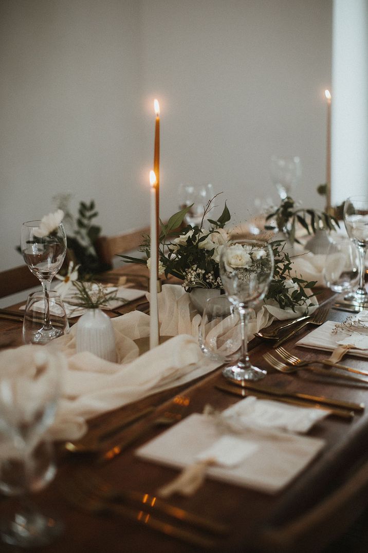 Neutral tone wedding tablescape with white table runner, neutral wedding flower arrangements and candles 