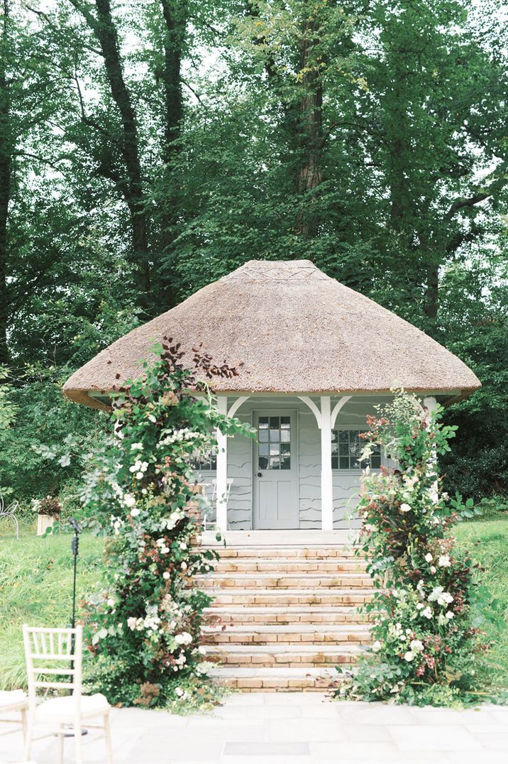 Outdoor wedding ceremony at Deer Park in Devon with vertical wedding flower arrangements decorating the altar