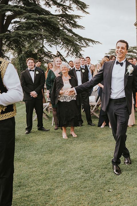 Bride in an off the shoulder wedding dress and groom in a tuxedo dancing in the grounds at Hedsor House with their Zaffa Band 