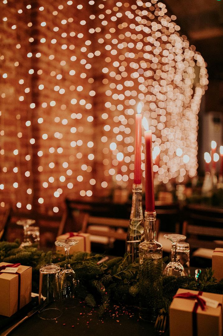 Red taper candles and green foliage with a backdrop of fairy lights