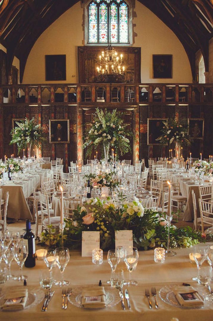 Reception room of Berkeley Castle wedding venue Cotswolds with white tablecloths, garden rose, dried flower and foliage wedding centrepieces, tapered candles, gold candlestick holders, festoon chandelier lighting and wooden beams 