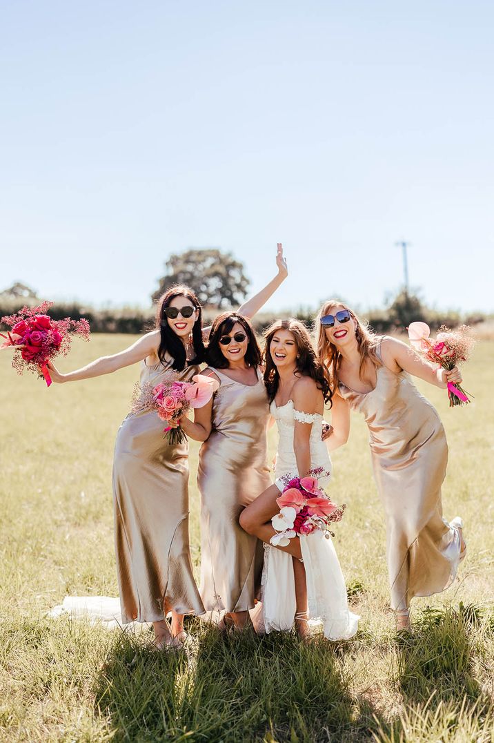 Bride in off the shoulder wedding dress posing with bridal party in gold satin bridesmaid dresses 