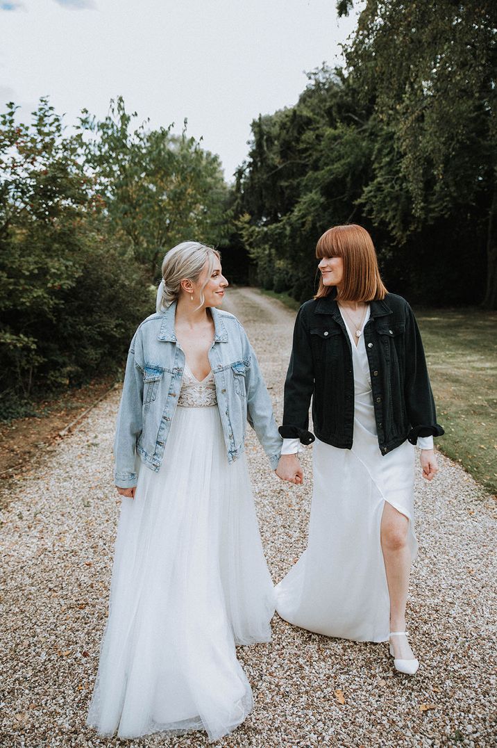 Bride in light blue denim jacket walking with bride in black denim jacket for LGBTQI+ barn wedding