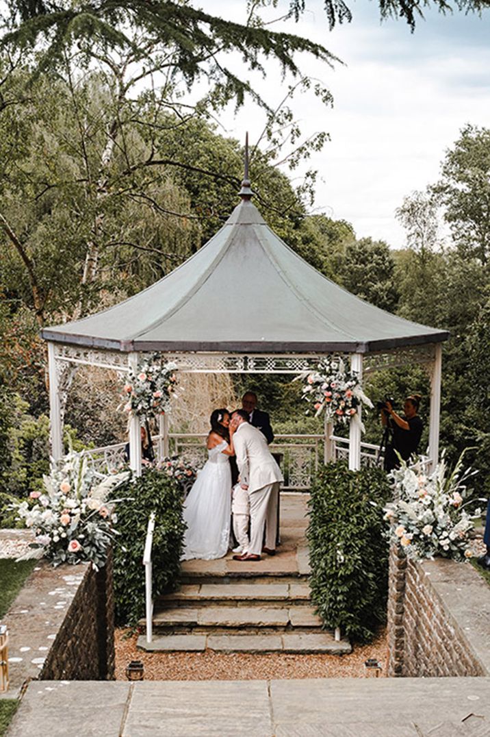 The bride and groom kiss at their outdoor gazebo at Pennyhill Park Hotel and Spa 