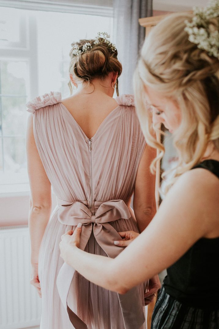 Wedding morning bridal preparations with bridesmaid in a pink chiffon dress having her satin bow tied up at the back 