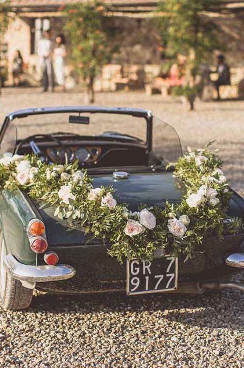 Classic green convertible wedding car with large floral wreath on boot