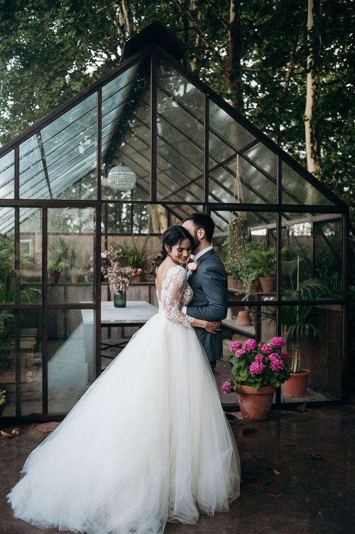 Bride in dramatic princess gown with long embroidered lace sleeves with groom in classic grey suit 