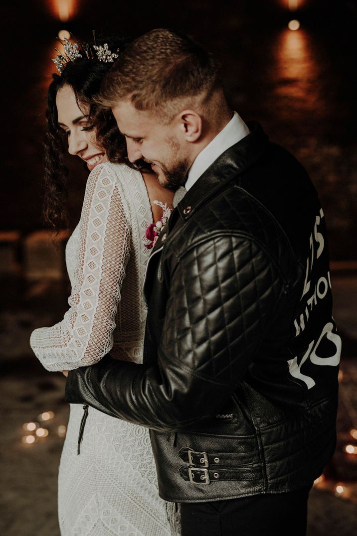 Groom in personalised leather jacket embracing the bride from behind in a lace wedding dress 