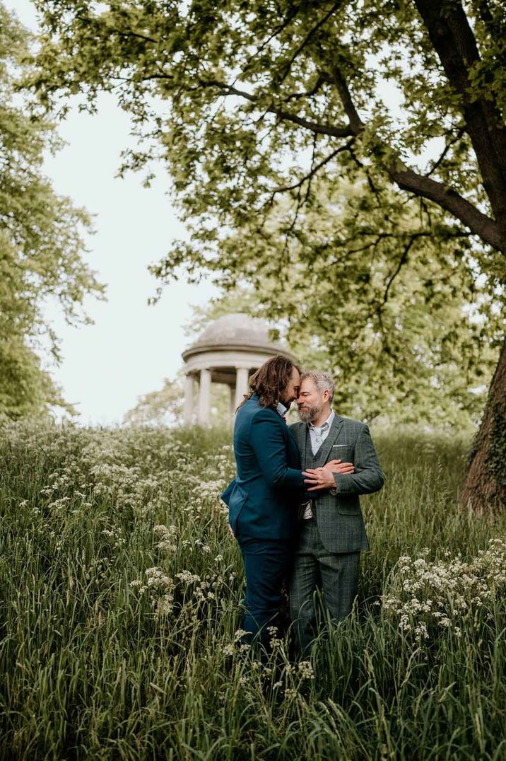 Grooms in three piece groom suits embracing on the grounds of Royal Botanical Gardens of Kew wedding venue 