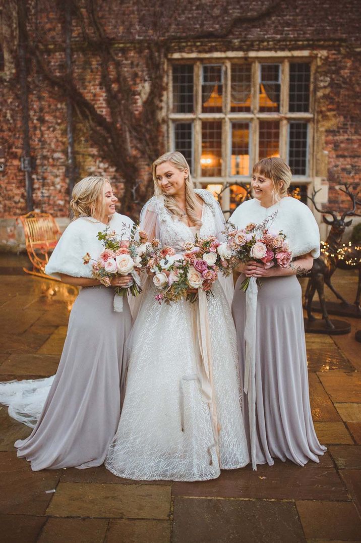 Bride wearing lace long sleeve wedding dress with bridesmaids in grey bridesmaid dresses and white bridal coverups at Goldsborough Hall 