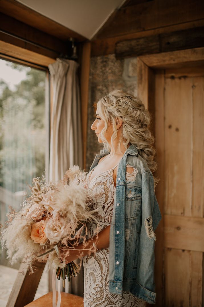 Bride with intricate braided wedding hair in lace wedding dress and light blue bridal denim jacket 