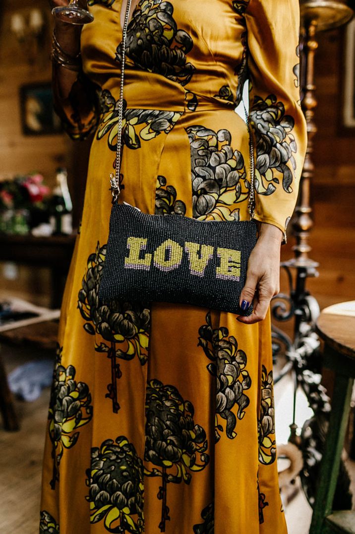 Bride in mustard yellow wedding guest dress with floral pattern and beaded love bag 