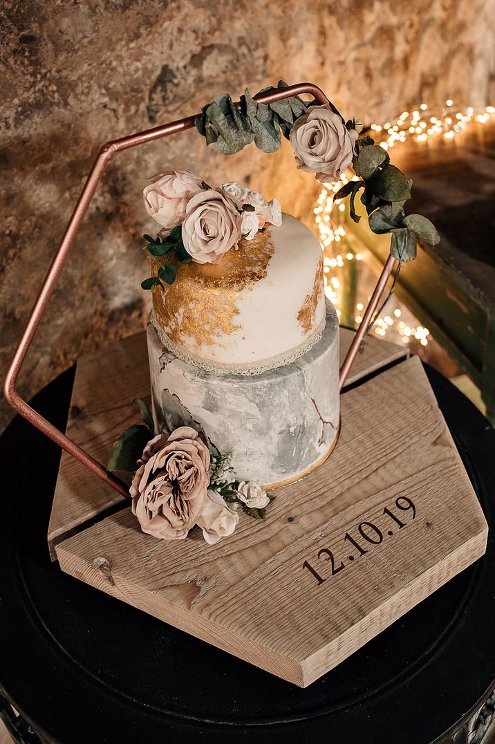 Two tier marble wedding cake on a wooden cake stand with hexagonal frame