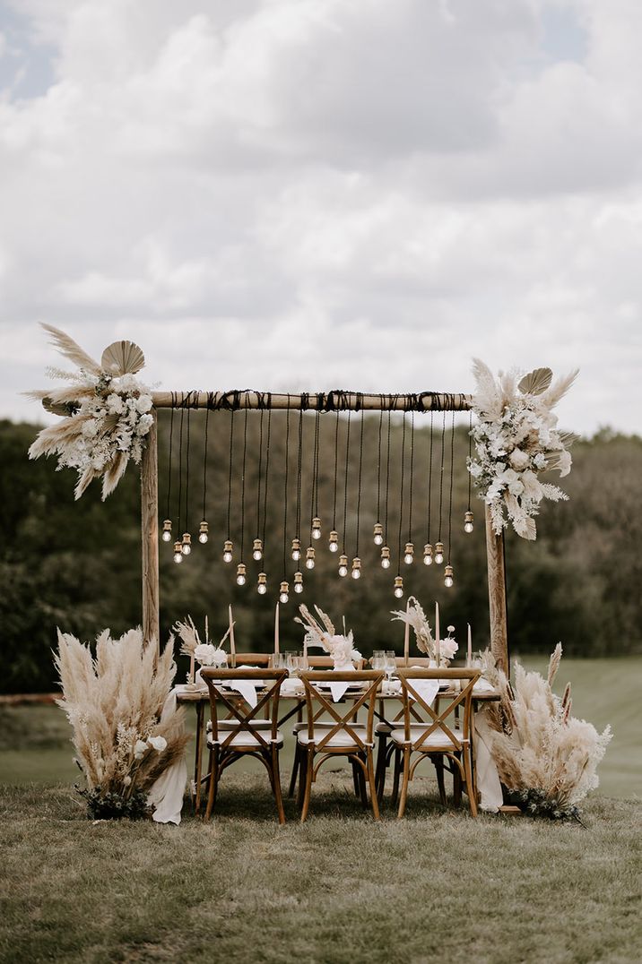 Outdoor wedding table setting with lots of dried grasses and festoon lighting 