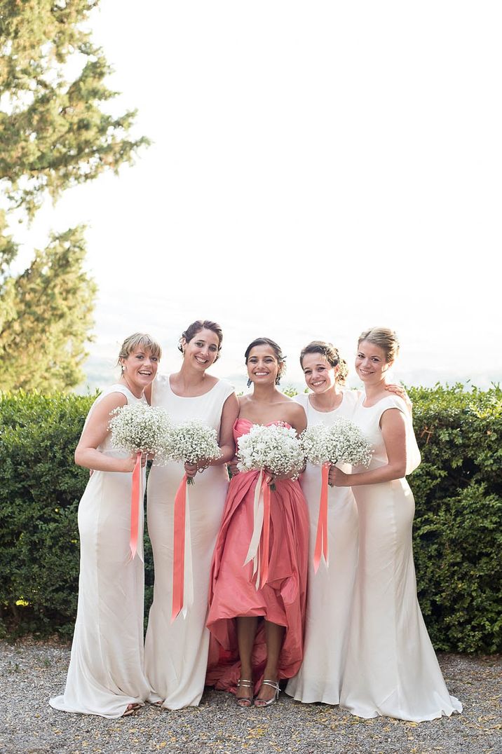 Bride in alternative pink wedding dress with bridal party in long satin white bridesmaid dresses and bouquets