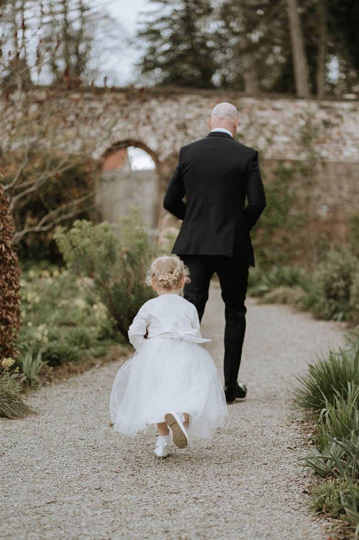 Young bridesmaid wearing white bridesmaid dress, white shoes, and a white cardigan 