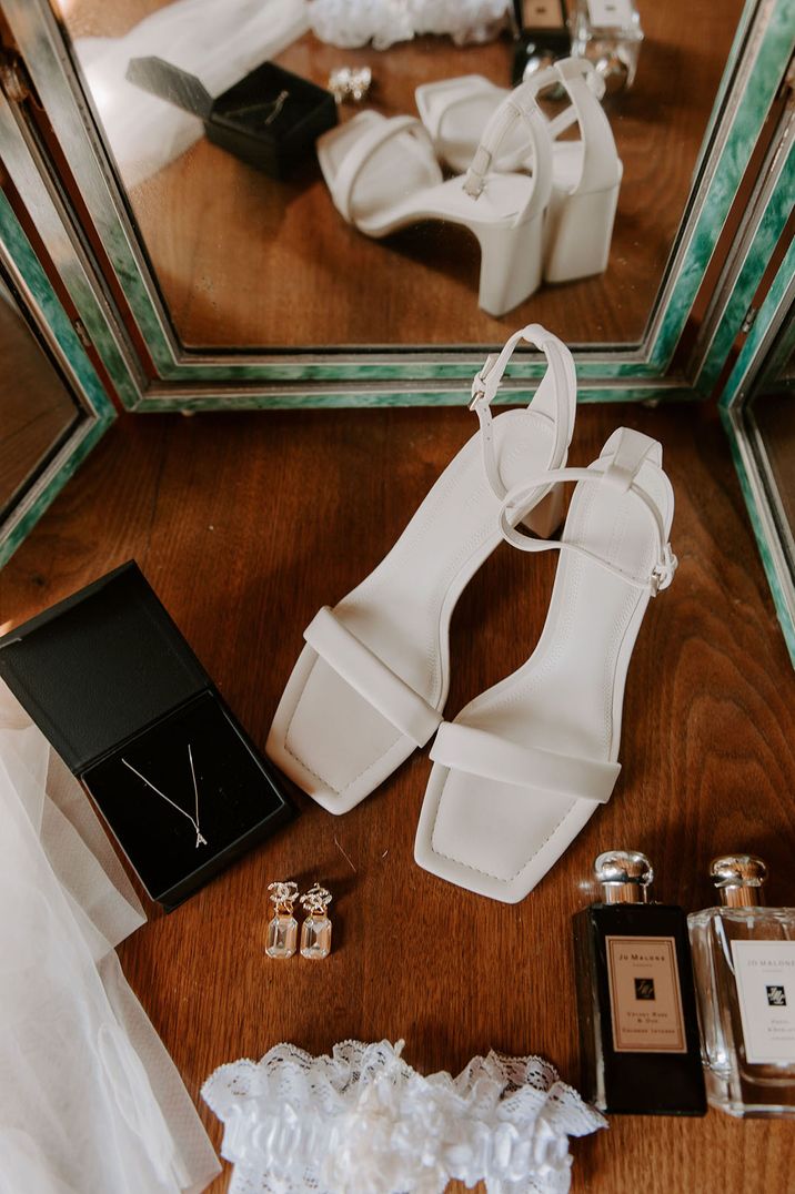 White strappy heels beside bridal perfume and garter