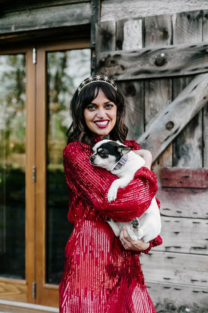 Bride in red sequin wedding reception dress with short brown hair and star tiara holding pet dog 