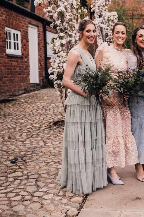 Bridesmaids in dainty light floral mismatched bridesmaid dresses holding mixed wildflower bouquets at greenery themed wedding