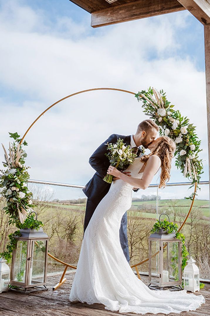 The bride and groom share their first kiss as a married couple with moon gate altar decoration 