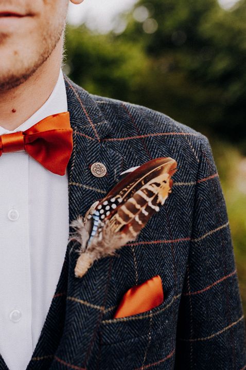 Groom in a navy wool suit with red check and a feather buttonhole 