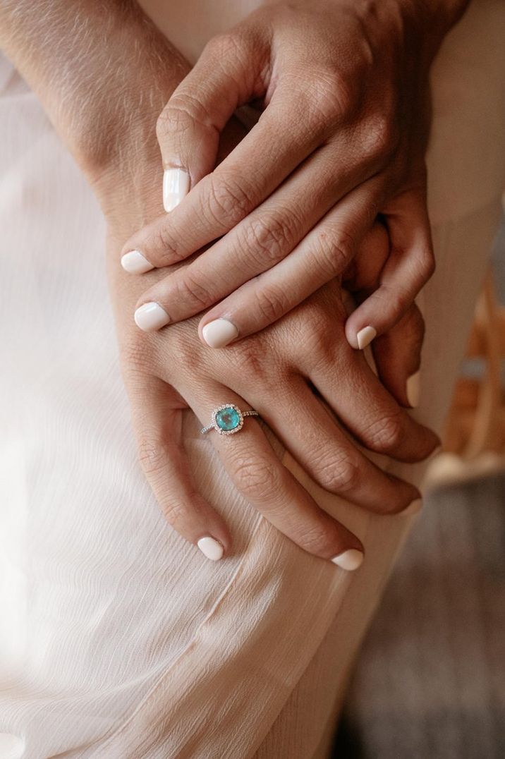 Bride with cream nail polish wearing a blue topaz engagement ring surrounded by diamonds 