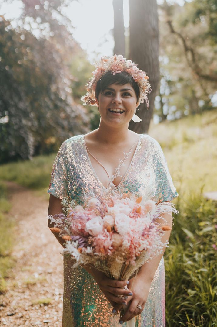 Bride with short dark hair wearing a sequin wedding gown with matching preserved flower bouquet and flower crown with roses and dried grass