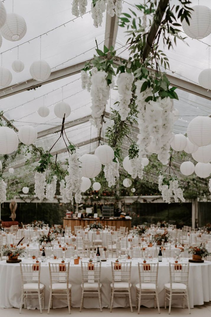 Wedding marquee reception decorated with white hanging lanterns and cascading white flowers 