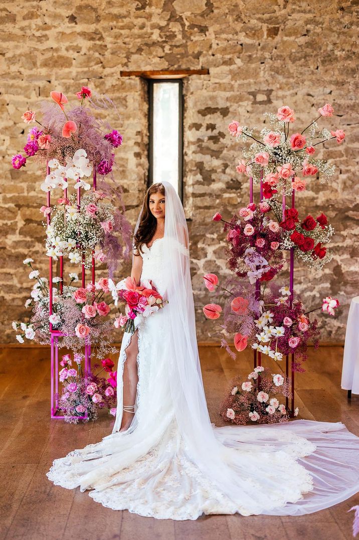 Pink wedding flower arrangements decorate the altar with the bride in an off the shoulder lace wedding dress with train 