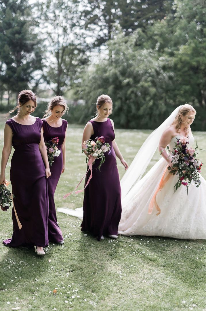 Bridesmaids in deep purple bridesmaid dresses walking along with the bride in a traditional princess wedding dress