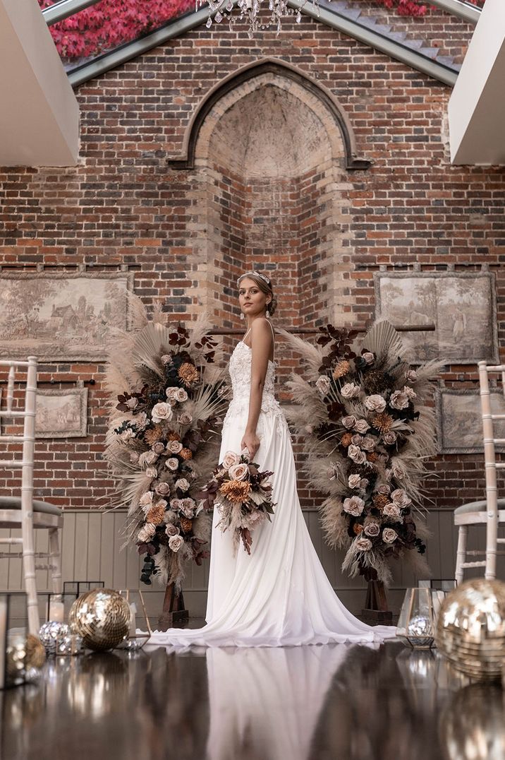 Orange and toffee roses flower columns with dried palm leaves decorating the aisle and altar 