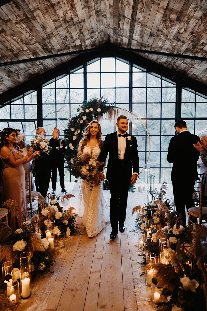 Groom in black tuxedo walking back down the aisle as a married couple with the bride in a sweetheart wedding dress 