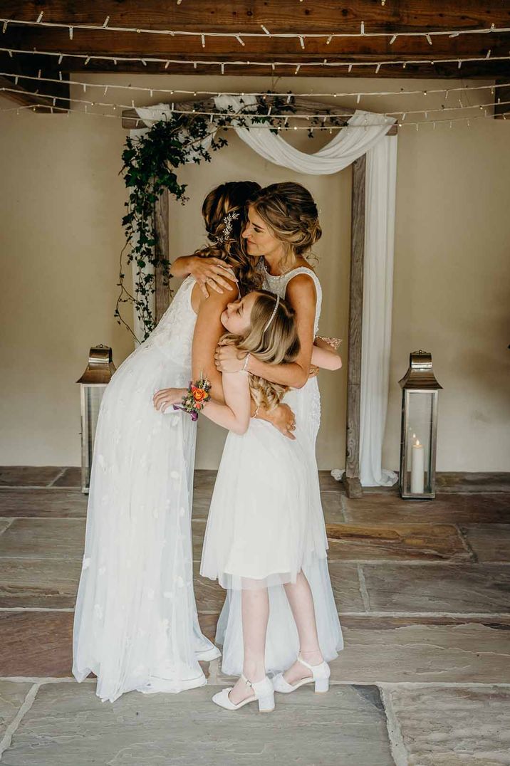 Same sex wedding ceremony at Ever After Wedding Venue with brides embracing their daughter during the nuptials 