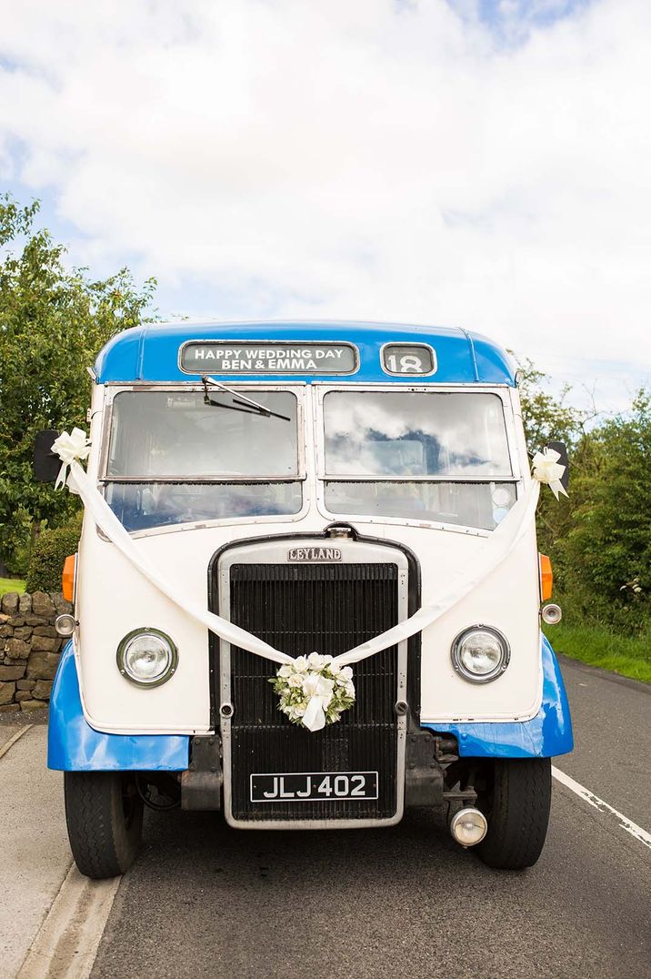 White and blue wedding bus with white ribbon and white floral wreath 