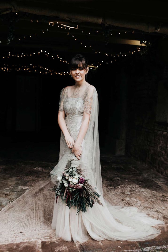 Bride in homemade sage tinted quarter length sleeve wedding dress with homemade bouquet with peacock feather detailing