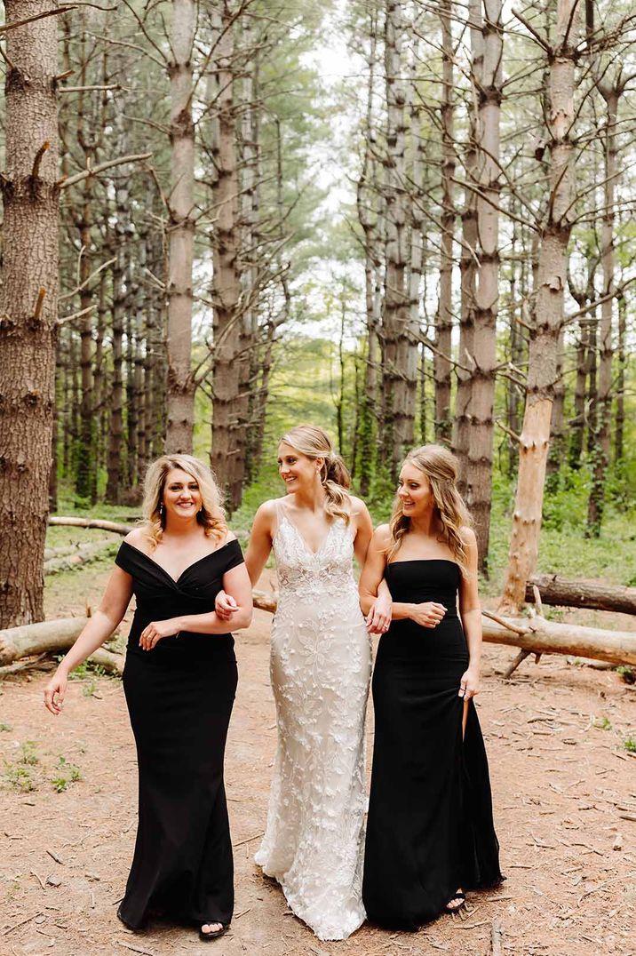 Bridesmaid wearing off the shoulder black bridesmaid dress and bridesmaid in strapless bandeau black bridesmaid dress with side split to leg