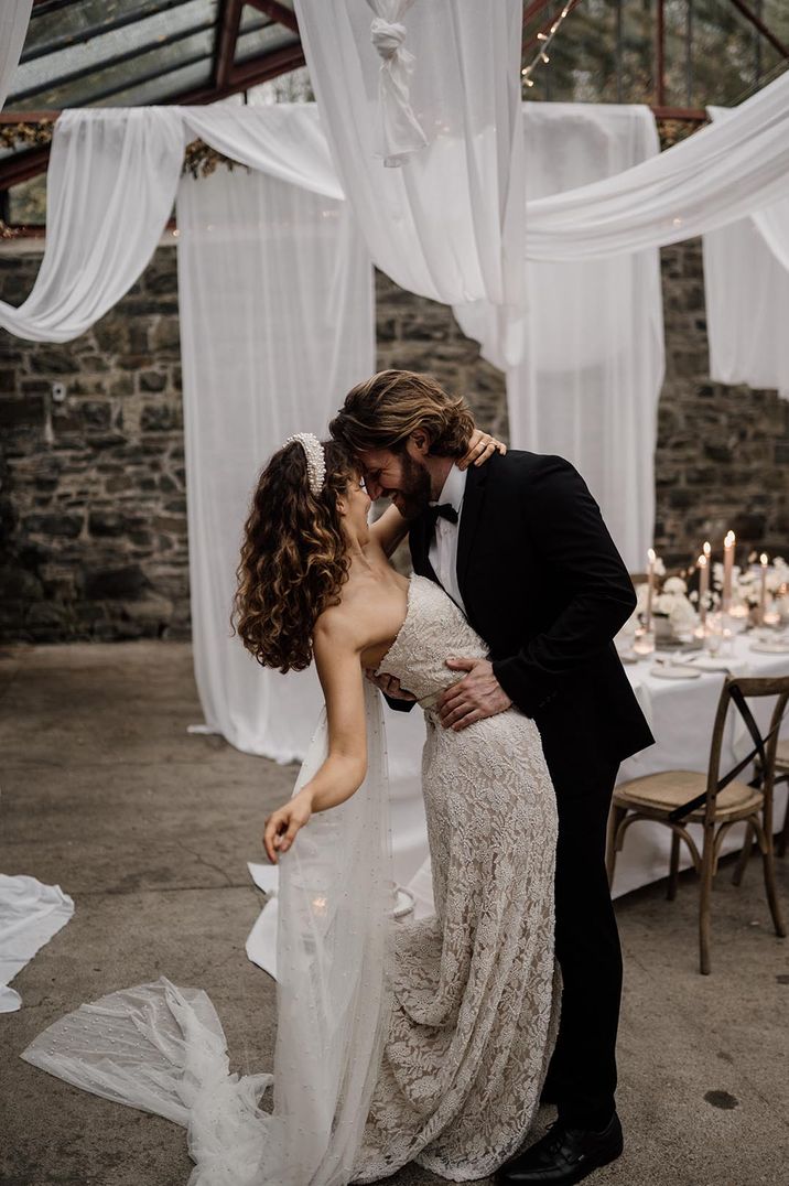 Bride in strapless lace wedding dress and groom in dark tuxedo embracing in Plas Dinam Country House glasshouse wedding venue 