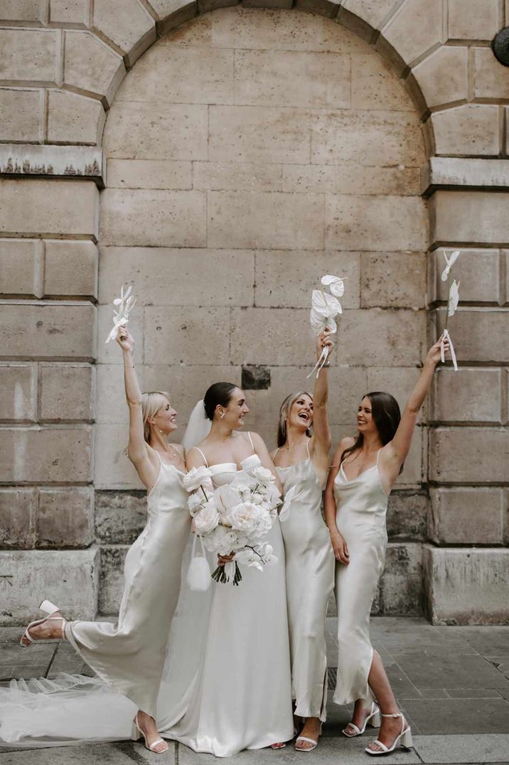 Bride in off shoulder satin wedding dress standing with bridesmaids in light green satin slip bridesmaid dresses 