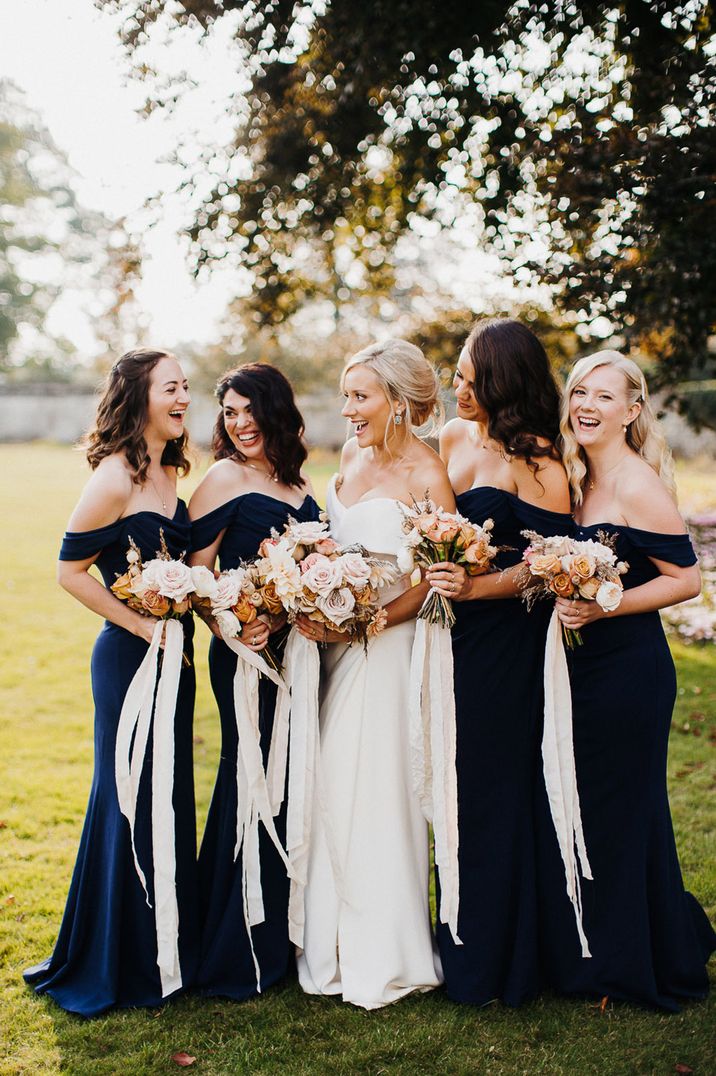 Bride in off the shoulder wedding dress with bridesmaids in navy blue dresses holding up bouquets