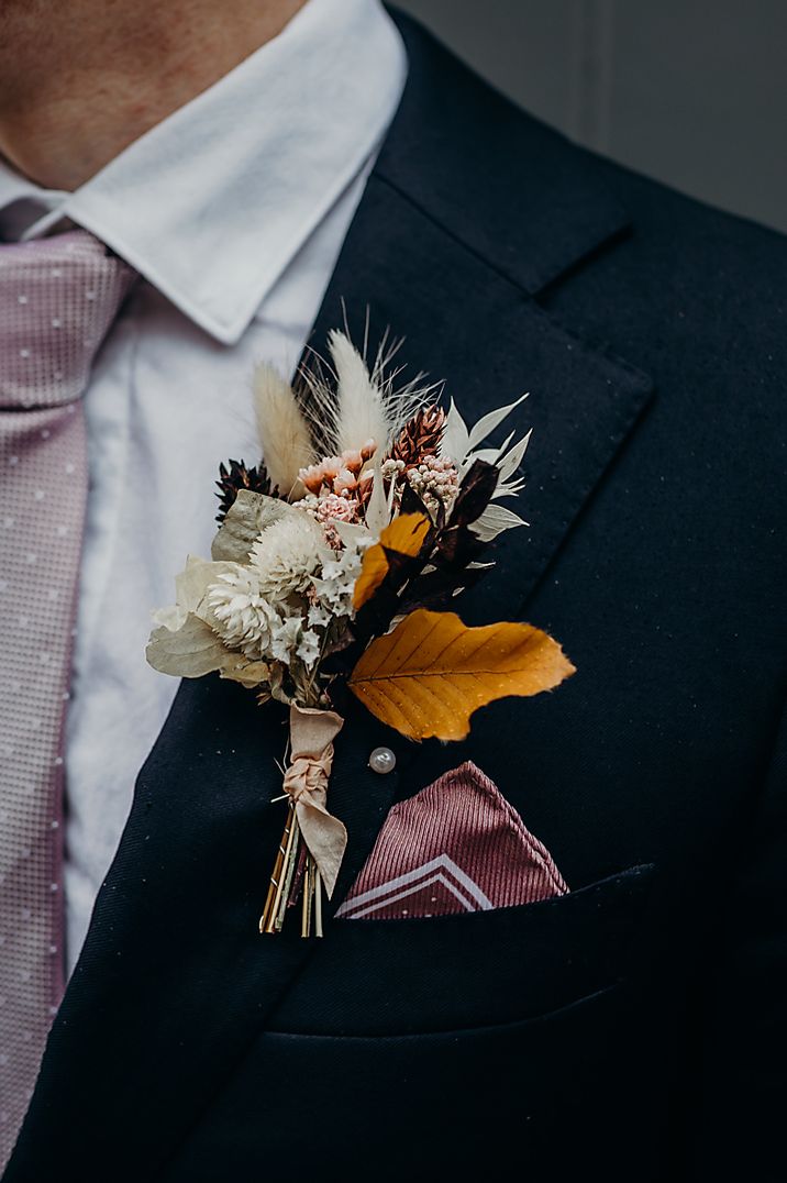 Groom in blue suit with a purple tie and dried flower buttonhole 