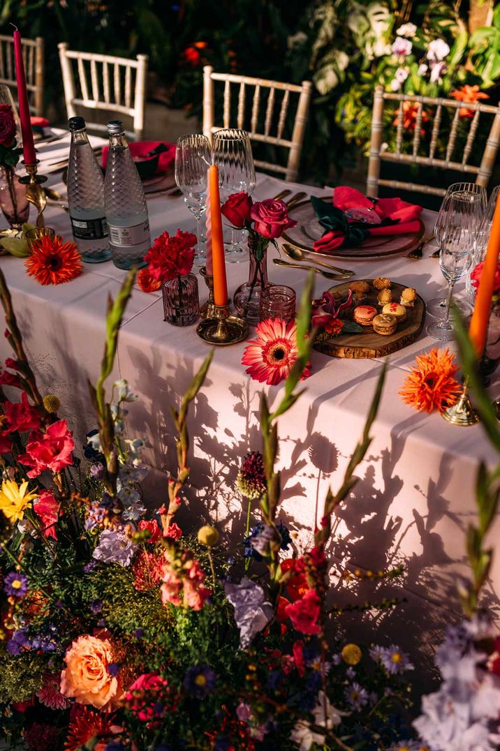 Outdoor wedding tablescape with pink tapered candles and pink, purple, yellow and red flower and foliage wedding arrangements 