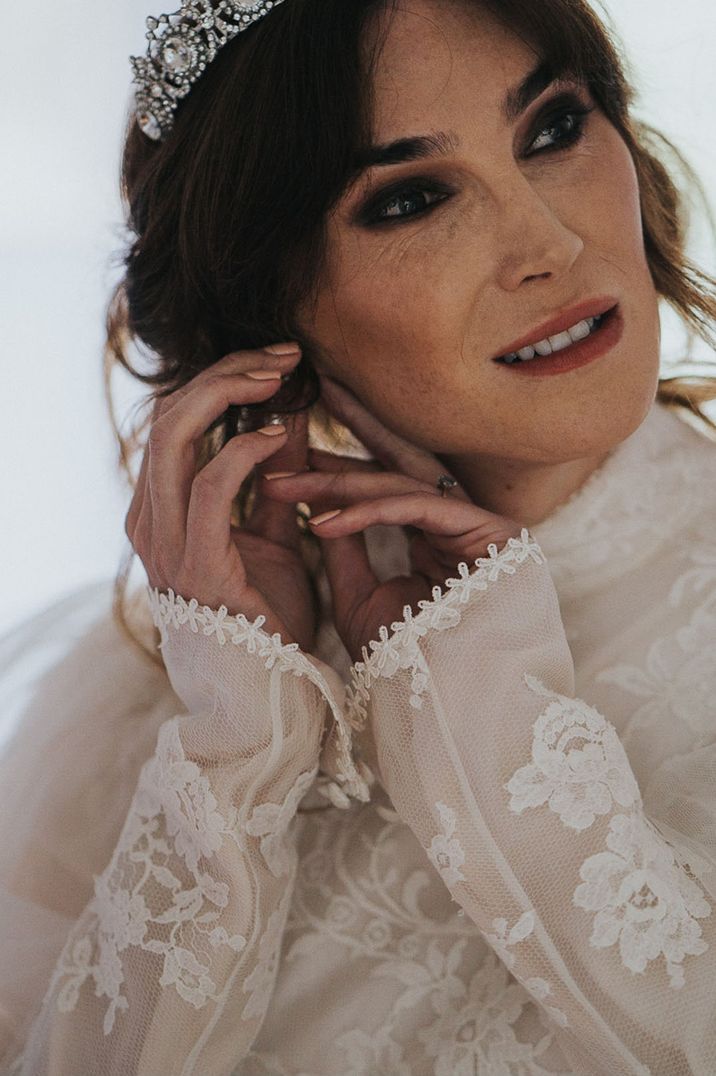 Juno Dawson putting on earrings as she wears long sleeved lace wedding gown with high neck and wedding tiara