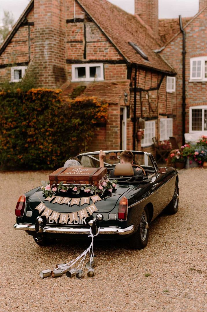 Black convertible wedding car with "just married" sign, suitcase, and tin cans decorations