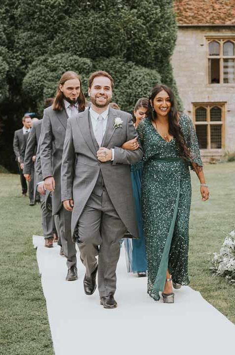 Mixed gender wedding party with groomswoman in bottle green sparkly gown walking down the aisle