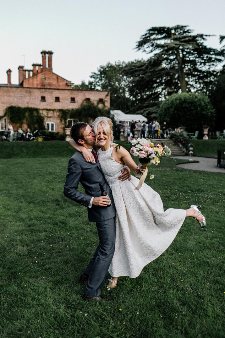 Bride in halterneck wedding dress and groom in dark suit embracing on the grounds of country house wedding venue Garthmyl Hall