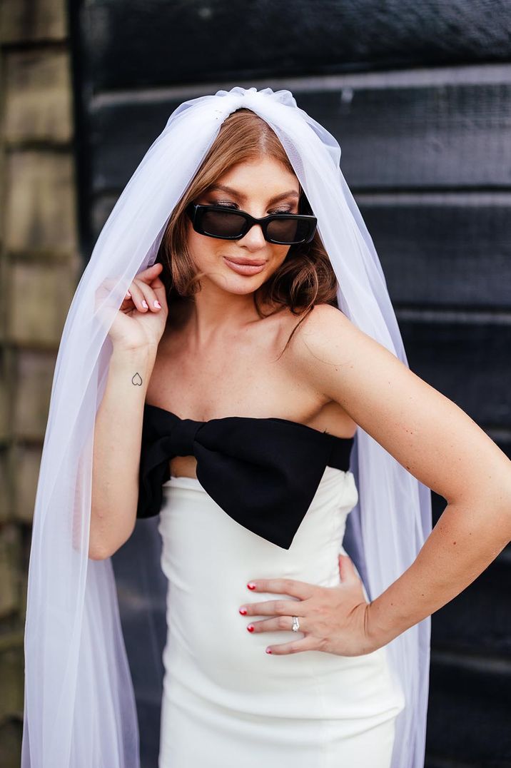 Bride in black and white bow wedding reception dress with cathedral length veil and black sunglasses 