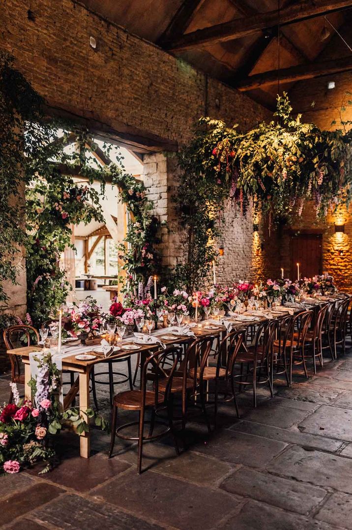 Cripps Barn wedding venue reception room wedding tablescape with pink and red garden roses, dried flowers and foliage, suspended foliage and tapered candles 