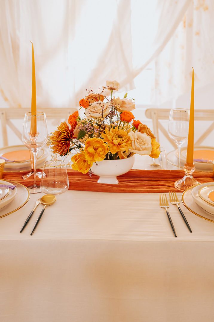 Orange autumnal wedding tablescape with sweetheart table decorated with table runner, taper candles and bowl arrangement 