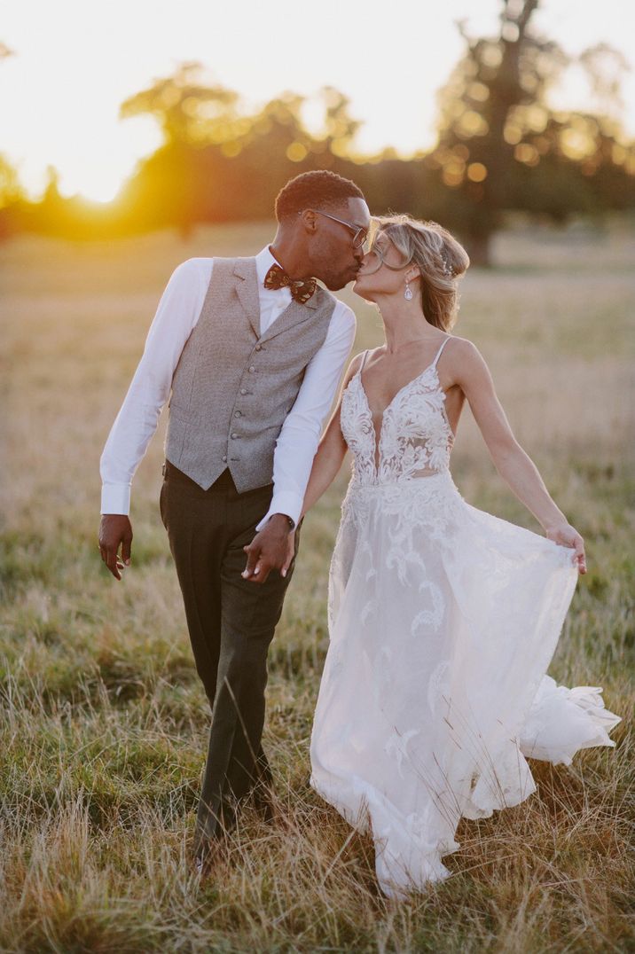 Golden hour portrait of groom in a grey waistcoat and bride in a tulle and lace wedding dress kissing